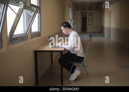 Young Asian man focused on laptop in hallway Stock Photo