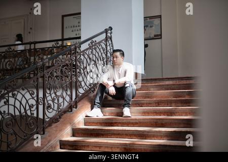 Thoughtful young man sits on a grand staircase Stock Photo
