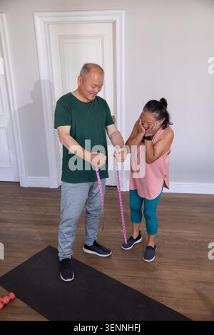 Asian Chinese couple standing and measuring with pink tape on exercise mat at home gym Stock Photo
