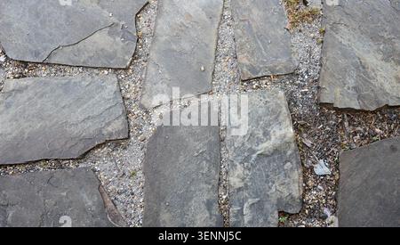 Flat slate stepping stone walk in a gravel and dirt bed with irregular gray stones and visible grass patches Stock Photo