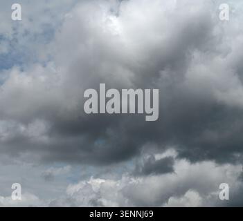 Horizontal close up of a mostly cloudy sky with a large dark storm cloud dominating the frame, scattered white clouds, and small blue patches Stock Photo