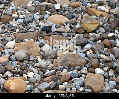 Horizontal close up of landscape river rock ground cover with mixed stone sizes and colors forming a rough uneven surface Stock Photo
