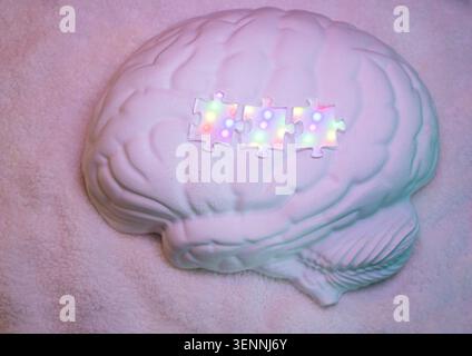White brain model features three colorful puzzle pieces on top, positioned on a soft textured surface, creating an intriguing visual composition Stock Photo