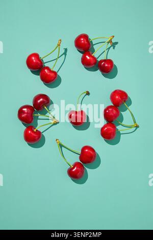 Ripe sweet cherries arranged on turquoise background with sunlight shadows, top view Stock Photo