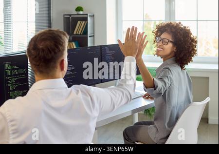 Programmers give high five after fixing code in bright tech office modern workspace Stock Photo