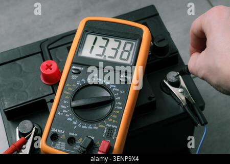 Check and charge car battery with charger. Person measures voltage. Selective focus an auto mechanic uses a multimeter voltmeter to check the voltage Stock Photo