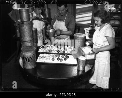 The press photograph records the preparation of Easter eggs and chocolate fish in 1936. Artisans are working on seasonal confectionery, documenting the manufacture of festive chocolate items associated with Easter celebrations. Stock Photo