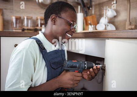 Handyman using cordless screwdriver repairing kitchen cabinet Stock Photo