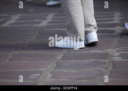 BANGKOK, THAILAND - MAY 23, 2026: Man in white shoes standing on stone courtyard, Lacoste shoes, high angle view Stock Photo