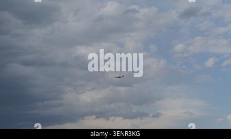 Airplane flying through a cloudy sky with varying shades of gray and blue clouds partially obscuring the sun, creating a dramatic and dynamic atmosphe Stock Photo