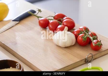 Cherry tomatoes on vine and whole garlic bulb sitting on wooden cutting board, knife resting Stock Photo