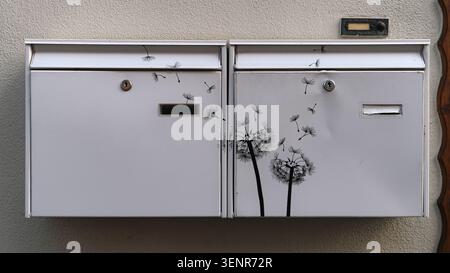 Two white wall-mounted mailboxes decorated with black dandelion seed stickers on a textured exterior wall. Stock Photo