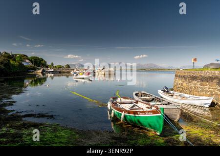 Boats resting on the harbor floor at low tide by Roundstone pier with the Twelve Bens mountain range in the background Connemara Ireland Stock Photo