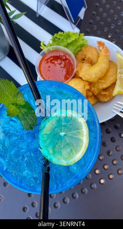 Blue cocktail with lemon and mint next to fried shrimp and sauce Stock Photo