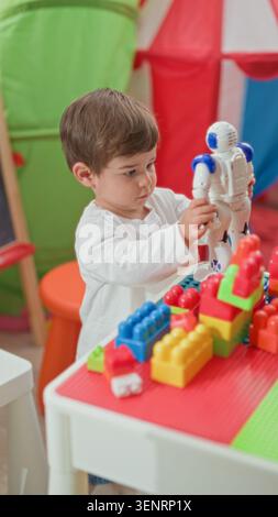 Boy holding white toy robot over a table with colorful building blocks in a playroom tent; curiosity imaginative play. Stock Photo