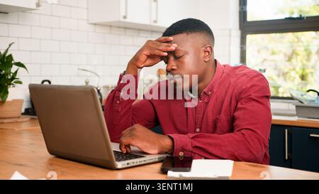Stressed Young Man Working On Laptop In Kitchen Home Office Rubbing Forehead Stock Photo