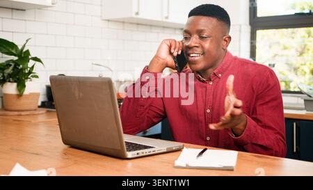 Young Man Working From Home Desk On Phone Call With Laptop And Notepad - Remote Business Conversation Stock Photo
