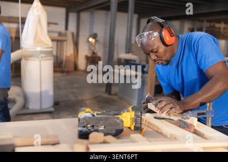 African American male woodworker in goggles smoothing timber using plane in workshop, copy space Stock Photo