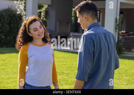 Couple standing and talking on green lawn by covered patio, woman wearing yellow headband Stock Photo