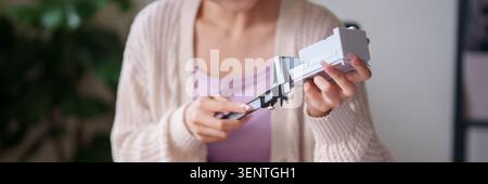 Adult woman using scissors to cut white paper furniture prototype at home workspace preparing design concept Stock Photo