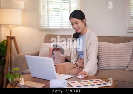 Young Asian female interior designer choosing upholstery samples while working from home on creative project Stock Photo