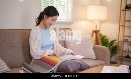 Asian woman examining colorful fabric samples and material swatches on sofa in bright contemporary home interior Stock Photo