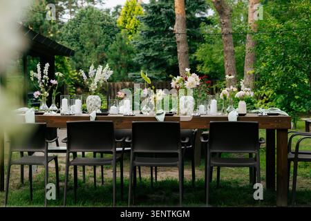 Elegant outdoor garden wedding reception table with wildflower centerpieces, white candles, sage napkins, and fairy string lights Stock Photo