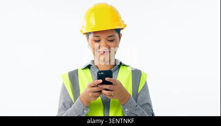 Engineering, woman and phone for construction chat, communication and project management in studio. Asian contractor or builder typing on mobile for Stock Photo
