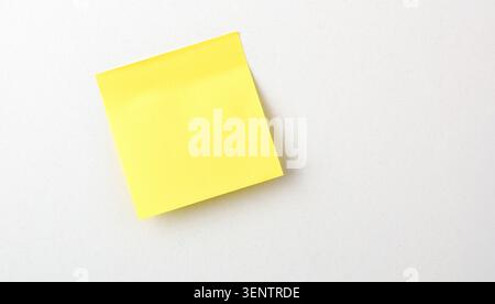 Single yellow sticky note placed on a clean white surface with copy space. Minimal office concept, top view, simple organization and reminder theme. Stock Photo