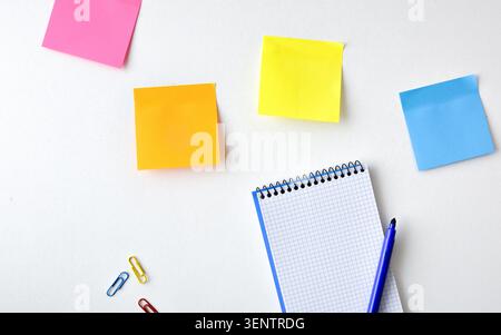 Top view of colorful sticky notes, a spiral notebook, pen, and paper clips on a clean white desk, representing organization, planning, productivity, a Stock Photo