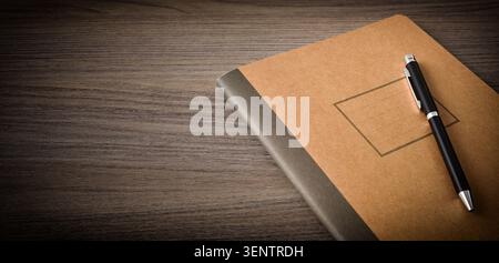 Brown notebook with a black pen placed on a wooden desk. Simple workspace composition with copy space, suitable for writing, planning, and business co Stock Photo
