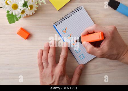 Close-up of a person marking completed tasks with an orange highlighter on a graph-paper notebook, symbolizing organization, productivity and planning Stock Photo