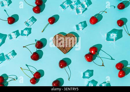 Sunlight summer day pattern made with fresh cherries, ice cubes and heart shaped chocolate on light blue background. Summer love concept. Flat lay. Stock Photo