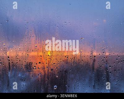 Water drops on the window at sunrise. Beautiful blurred picture of sunset through foggy glass. Abstract background. Soft focus. Artificial noise Stock Photo