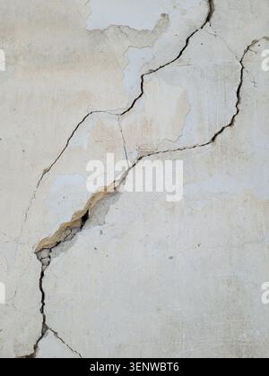 Two diagonal cracks on old white worn concrete wall. Earthquake effects. Selective focus. Stock Photo