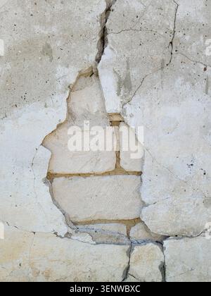 Cracks and a hole in the plastered surface of the wall of an old stone building. Destruction after an earthquake. Close-up. Copy space Stock Photo