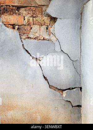 Cracks and a hole in the plastered surface of the wall of an old brick building. Huge big crack between walls due to humidity. Stock Photo