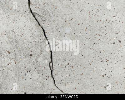 Cracked concrete surface covered with gray cement mortar. Destruction after the earthquake. Vertical uneven crack in the wall. Copy space. Stock Photo