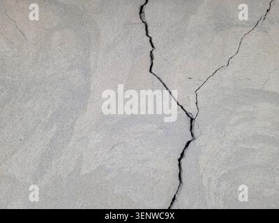 Cracked concrete surface covered with gray cement mortar. Destruction after the earthquake. Rough winding cracks on the wall. copy space. Texture Stock Photo