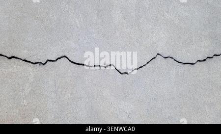 Cracked concrete surface covered with gray cement mortar. One long, winding crack in the wall. Destruction after the earthquake.  Copy space. Texture Stock Photo