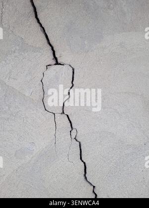 Vertical uneven crack on the wall. Cracked concrete wall covered with gray cement mortar. Destruction caused by an earthquake. copy space. Texture Stock Photo