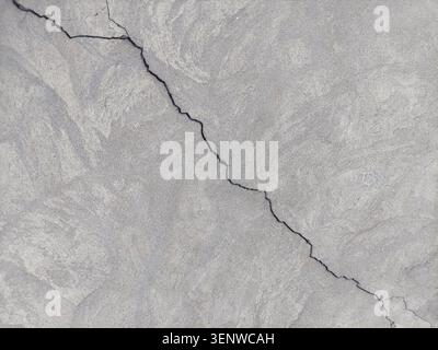 Large diagonal uneven crack in the wall. Destruction caused by an earthquake. Cracked concrete wall covered with gray cement mortar. copy space. Stock Photo