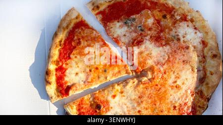 Top view of a fresh, hot classic Margherita pizza with melted molted mozzarella in a cardboard delivery box, with one slice separated. Overhead view. Stock Photo