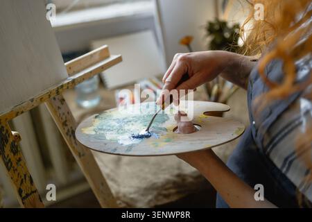 Closeup process of mixing colorful paint with spatula on artist palette in creative workshop. concept of painting, art and handmade artwork. Stock Photo