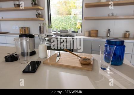 Wooden cutting board is holding glass bowl of peanut butter and spoon on countertop beside blender Stock Photo