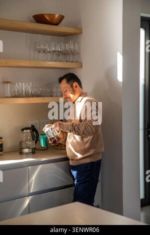 Mature Asian man standing at kitchen counter pouring coffee from French press into green mug Stock Photo