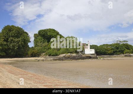 The historic white bathing house nestled in green trees on the sandy coastline at Penrhos Coastal Park, Isle of Anglesey, North Wales. Stock Photo