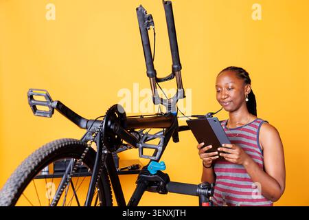 Female holding a tablet and inspecting damaged bike components, with active sporty woman using smart digital device to research bike repair instructions. Stock Photo