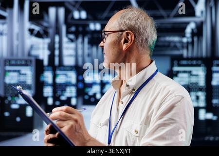 Elderly engineer in crypto mining farm with specialized hardware using blockchain technology, with fintech expert holding clipboard, inspecting asic rigs solving complex computational problems. Stock Photo