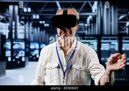 Senior developer immersed in virtual reality at data center, doing hardware maintenance, with professional using VR headset to optimize server rows system performance, harnessing advanced technology. Stock Photo